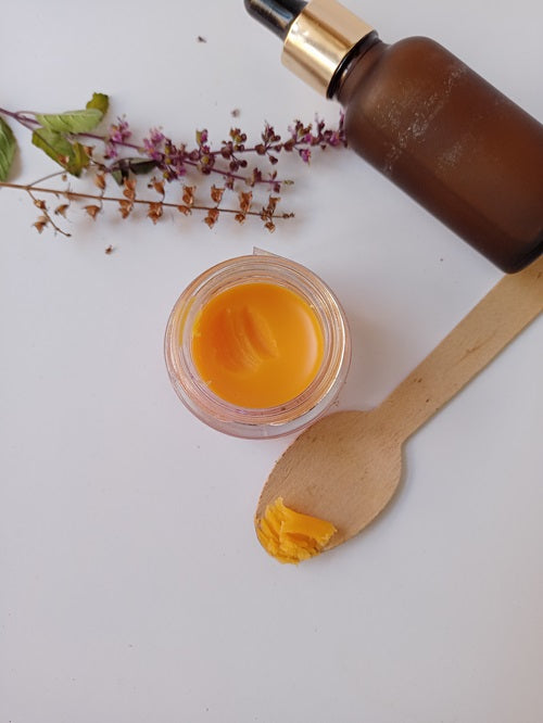 Yellow mango lip balm jar with a little scooped out on a wooden spoon