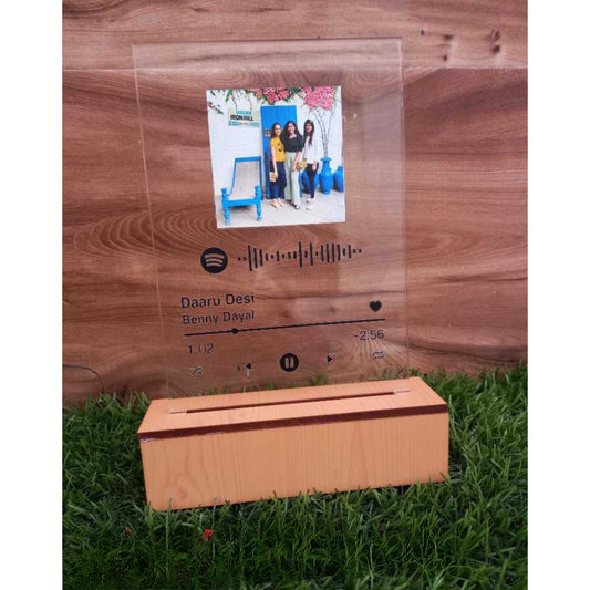 Glass like frame with people's photo, spotify song link and wooden base kept on green grass
