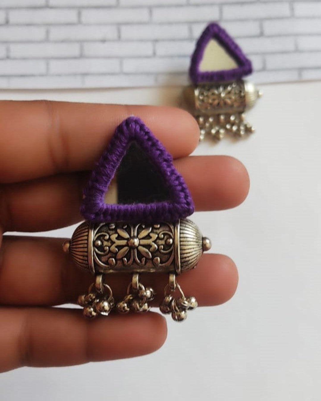 Palm holding Triangular purple and silver mirror studs jhumka earrings on white grey backdrop