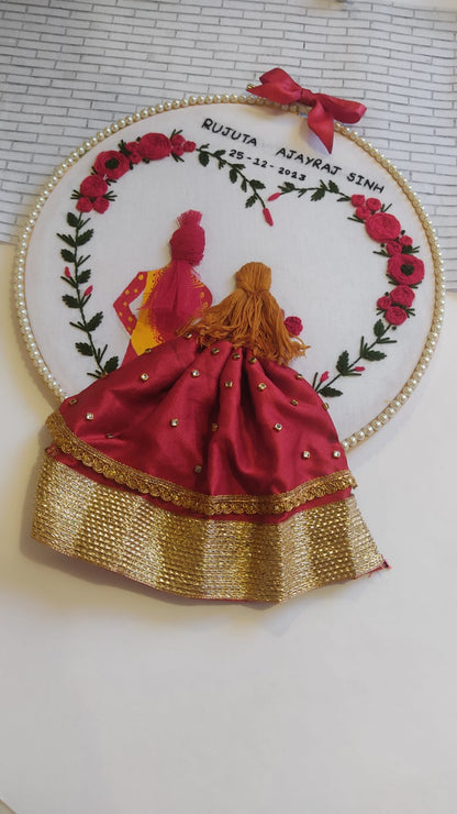 Round embroidery hoop art with bride in red lehenga, groom in yellow outfit and floral design on sides