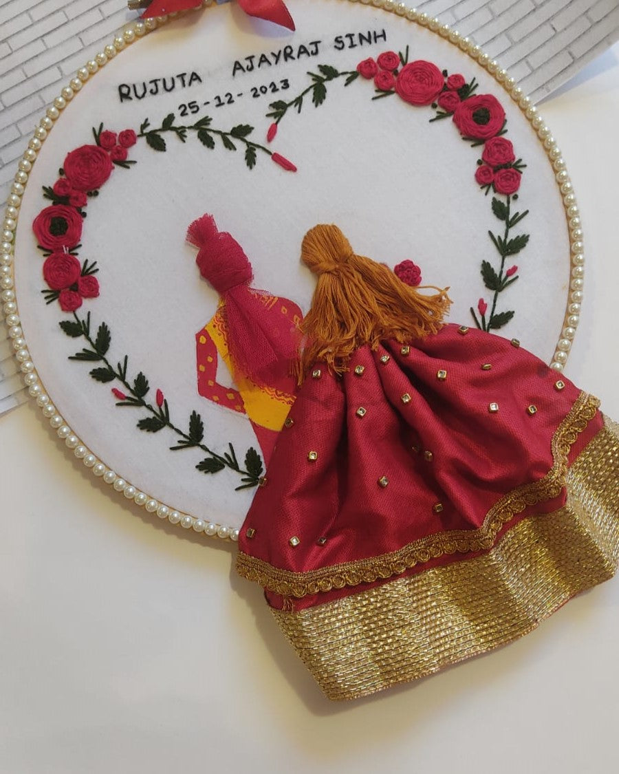 Round embroidery hoop art with bride in red lehenga, groom in yellow outfit and floral design on sides