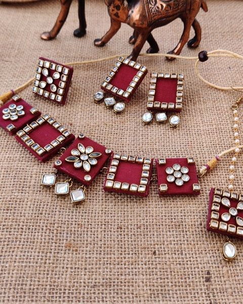Red wine choker necklace earrings mangtika set with white kundan borders on jute background