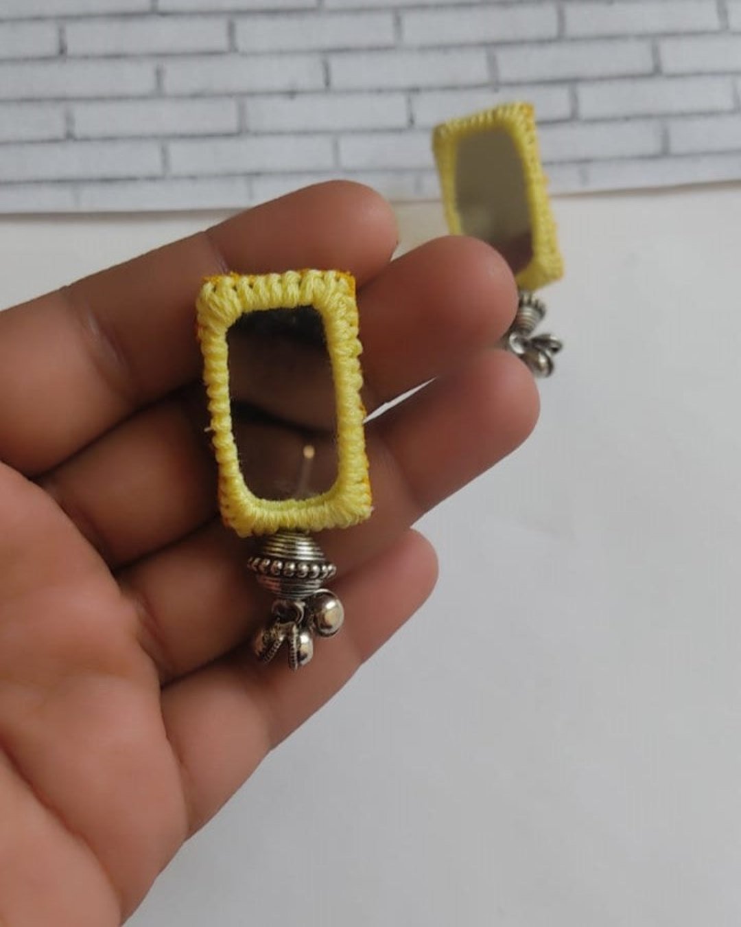 Palm holding Yellow rectangular mirror earrings with ghungroos on white backdrop