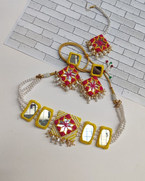Yellow necklace and earrings set with white and golden beads on white backdrop