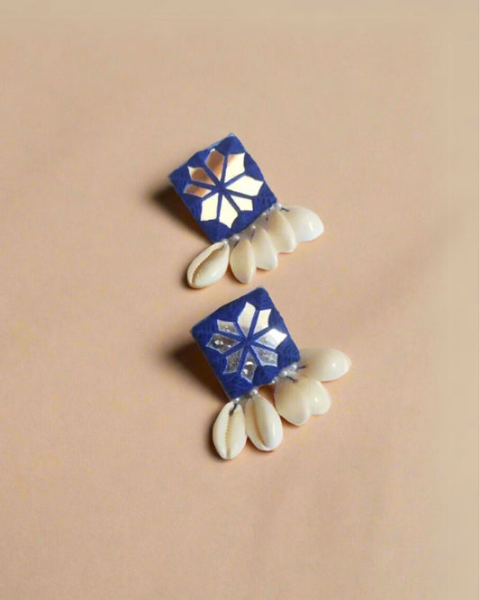 A pair of royal blue square mirror shell stud earrings with a floral pattern and white shell accents displayed against a beige background.