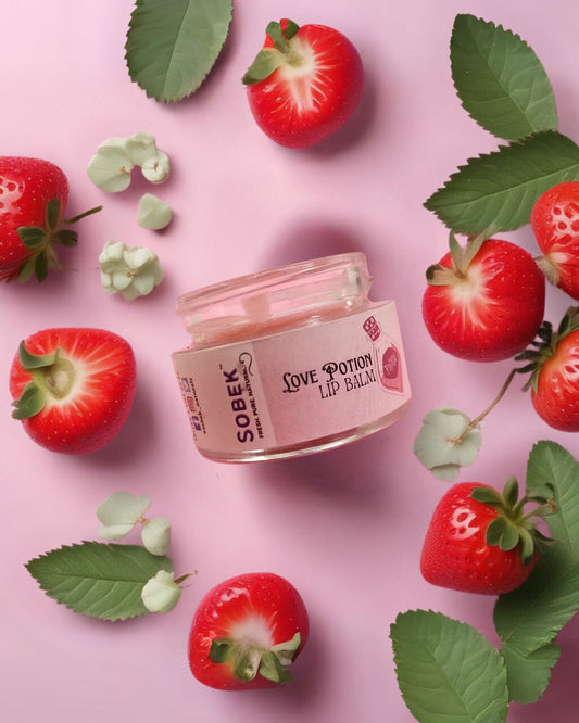 Sobek naturals strawberry lip balm in glass jar with pink backdrop and some strawberries around it