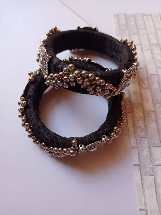 Two Black bangles with silver details on them on a white grey backdrop