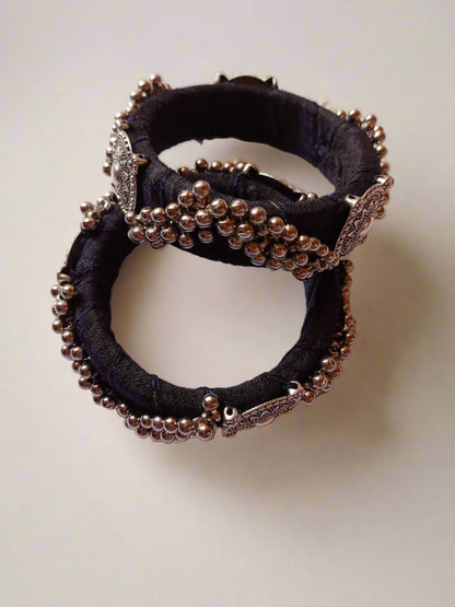 Two Black bangles with silver details on them on a white grey backdrop