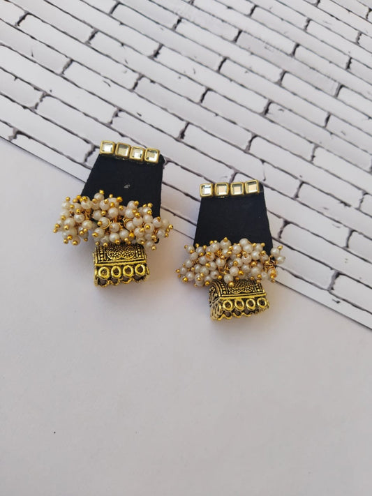 Black mini earrings with golden charms and white beads on white grey backdrop