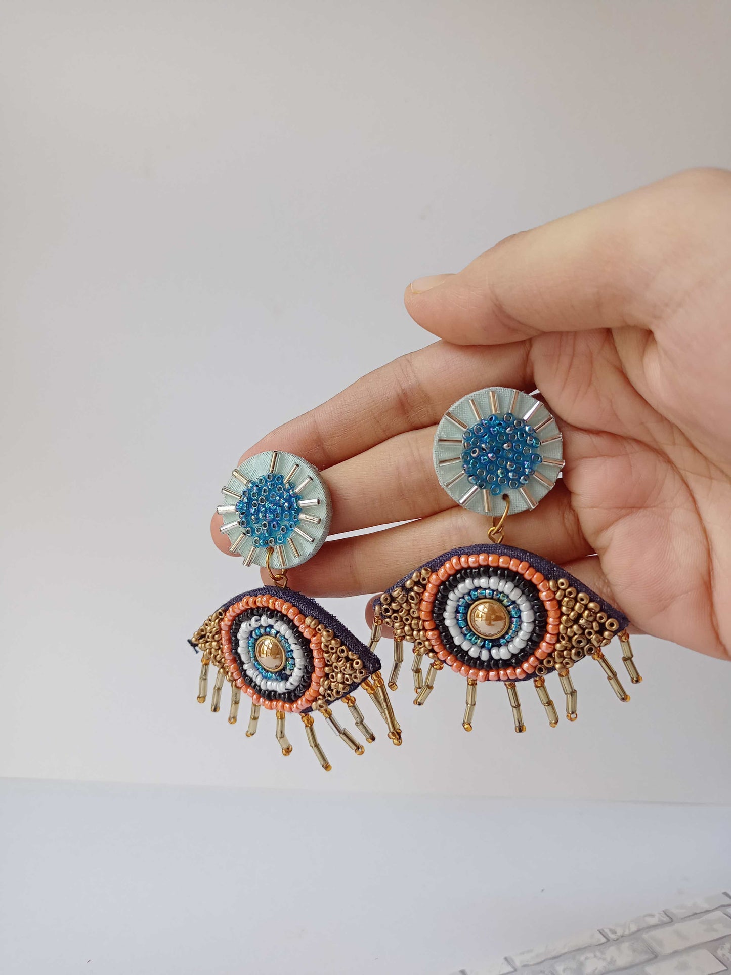 Palm holding Blue, black and white evil eye beaded earrings on white grey backdrop