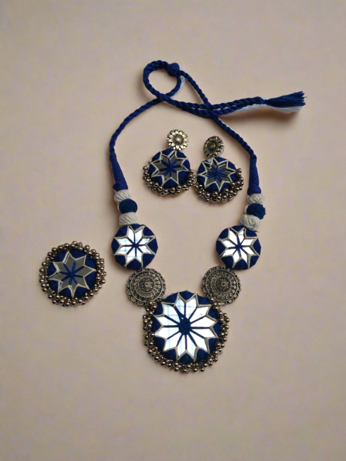 Blue necklace and earrings with mirror and silver charms on white backdrop