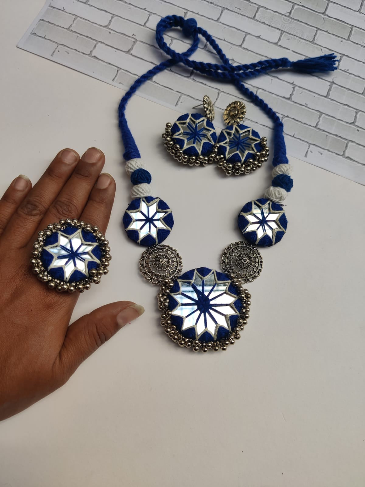 Blue necklace and earrings with mirror and silver charms on white backdrop