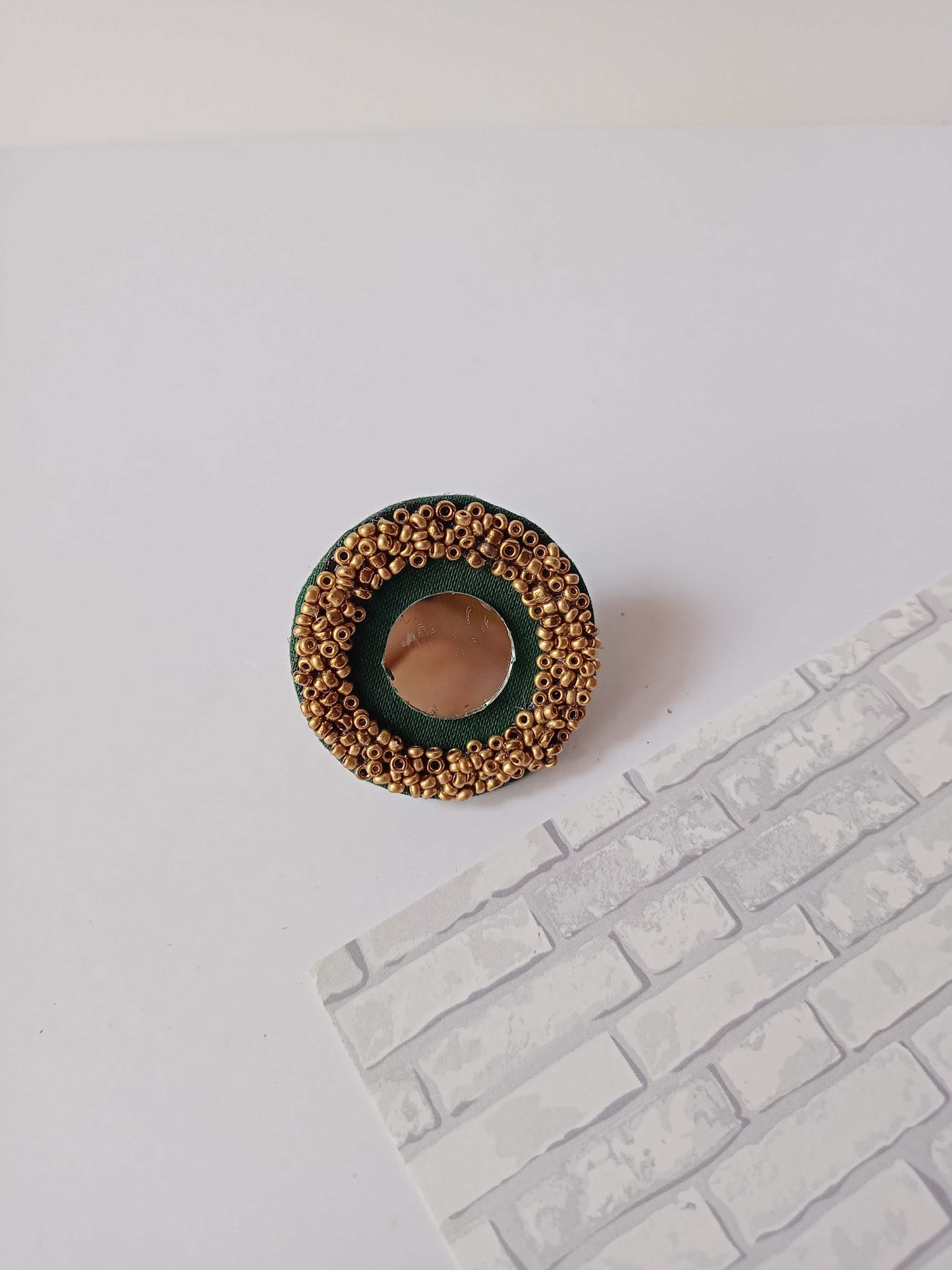 Dark green round finger ring with mirror and golden beads border on white backdrop