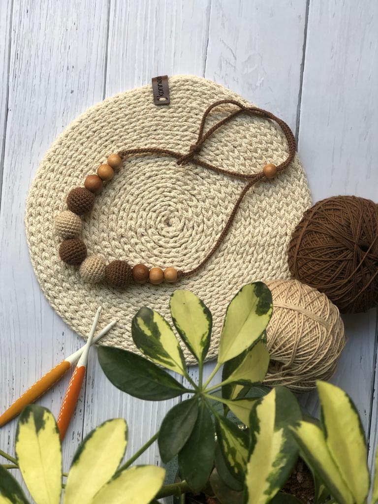 Brown and light brown crochet round necklace on white crochet base with threads in backdrop