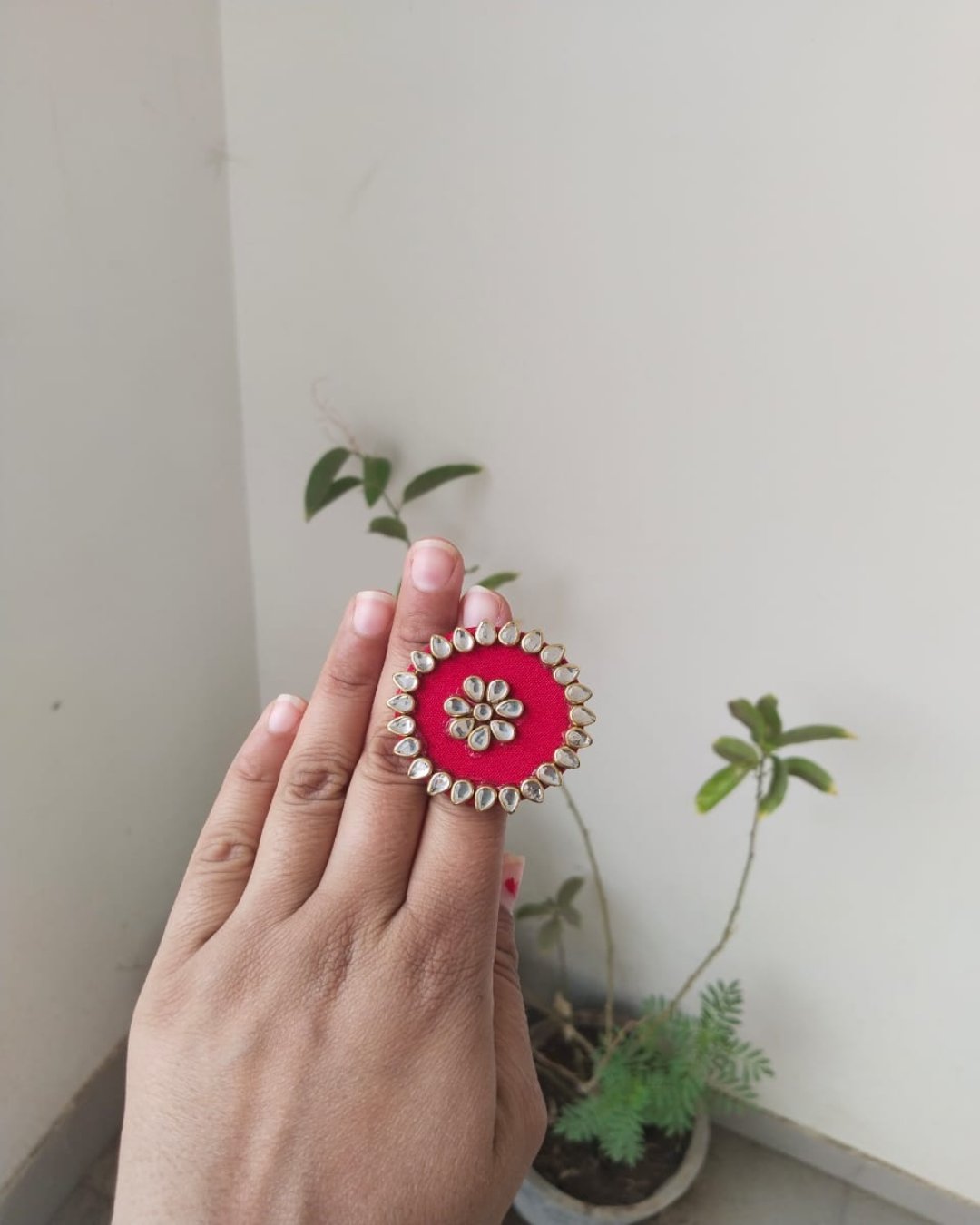 Palm wearing red round finger ring with kundan border on white backdrop