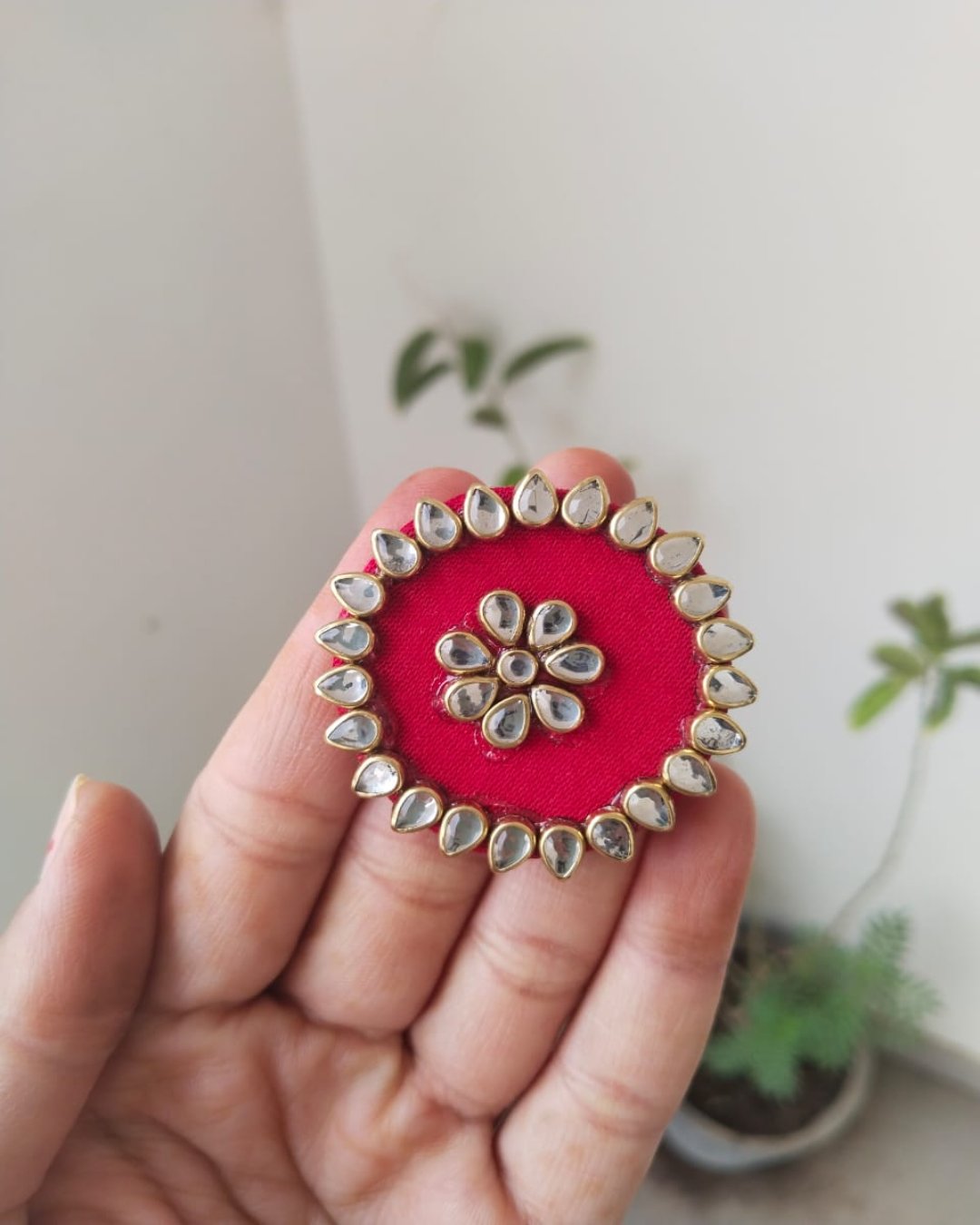 Finger holding red round finger ring with kundan border 