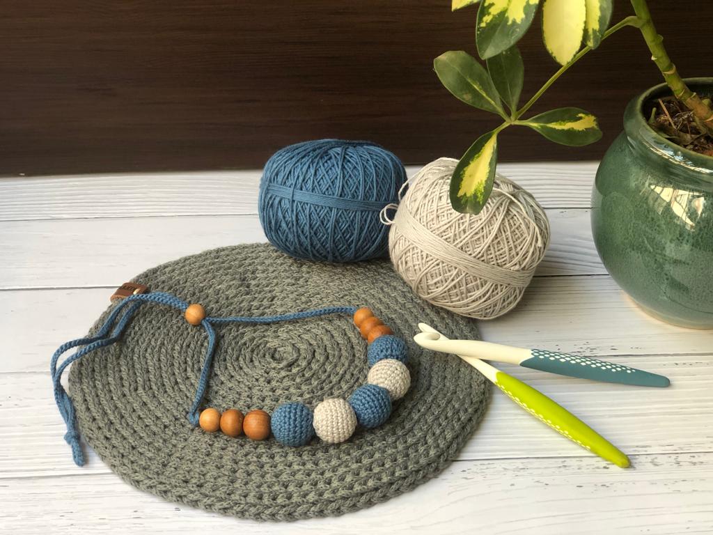Dark blue and white crochet necklace with wooden beads on grey crochet base with wool props