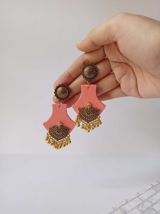 Hand holding peach pink earrings with golden charm on white backdrop