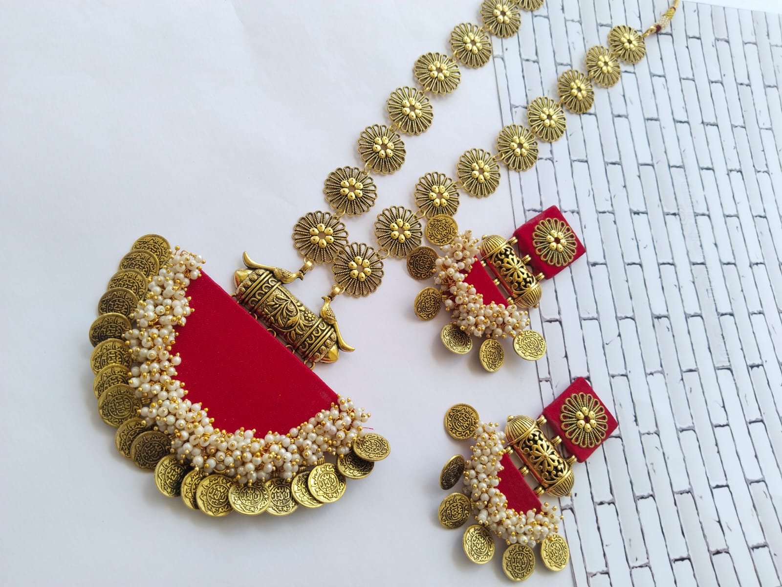 Hot red long necklace with semi round locket and golden chain with matching earrings on white backdrop