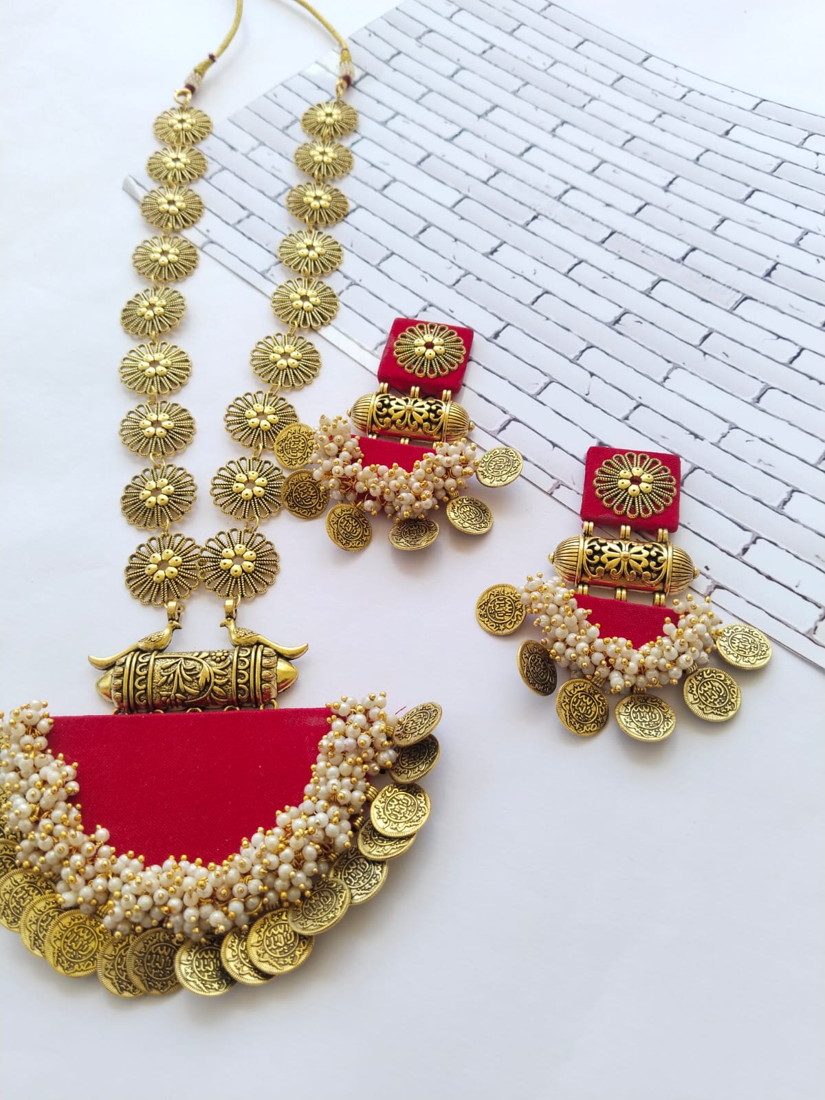 Hot red long necklace with semi round locket and golden chain with matching earrings on white backdrop