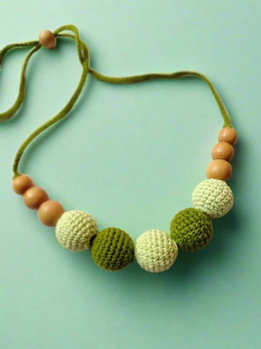 Light and dark green crochet necklace with wooden beads on white grey backdrop