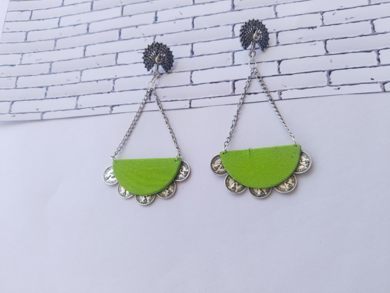 Light green and silver chain earrings with silver coins details at bottom on white backdrop