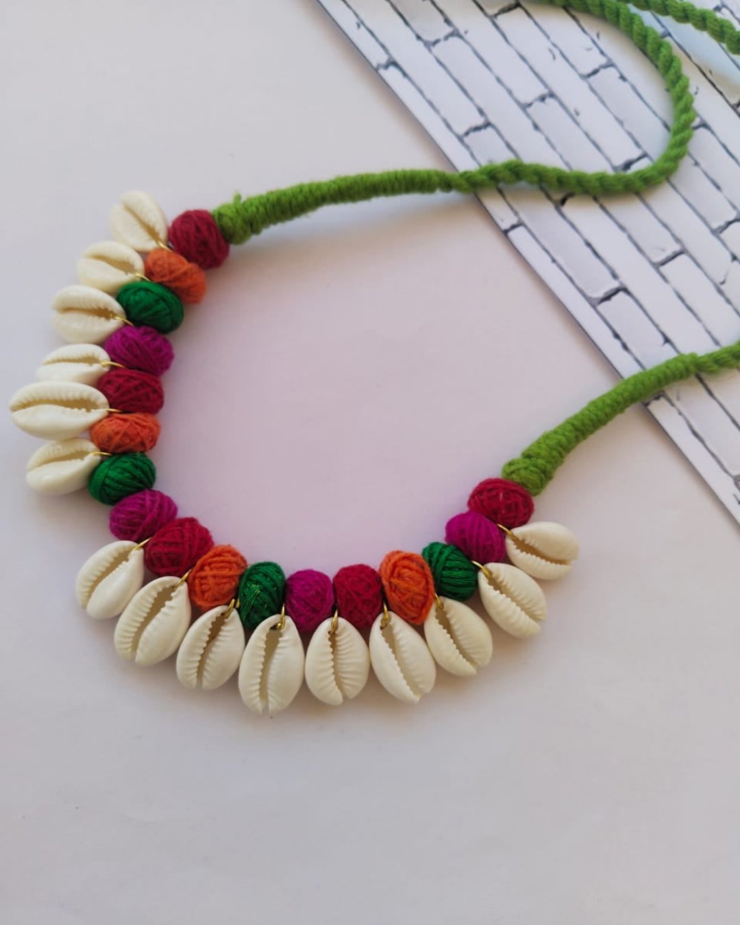 Multicolor pom pom necklace with white sea shells on white backdrop