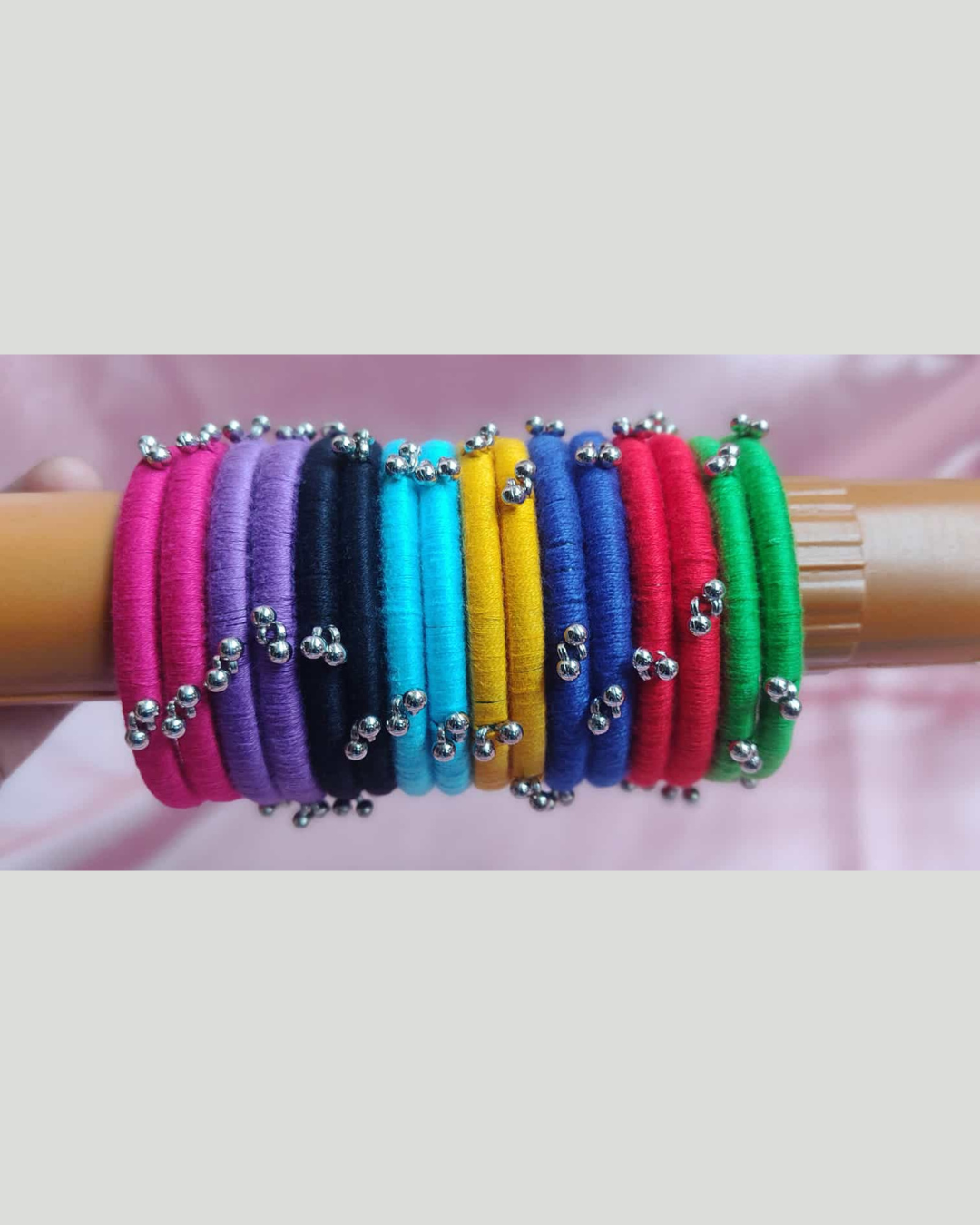 Multi color bangles on wooden stick on a pink backdrop