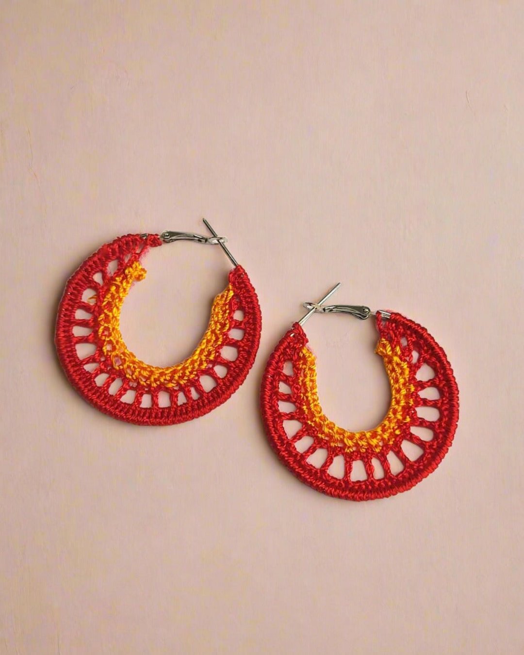 Orange and yellow crochet hoops earrings on white grey backdrop