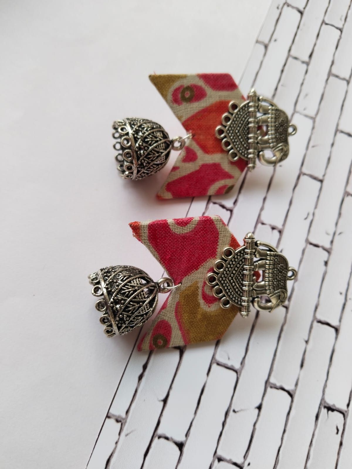 Orange printed earrings with silver jhumka and elephant charm on top on white backdrop