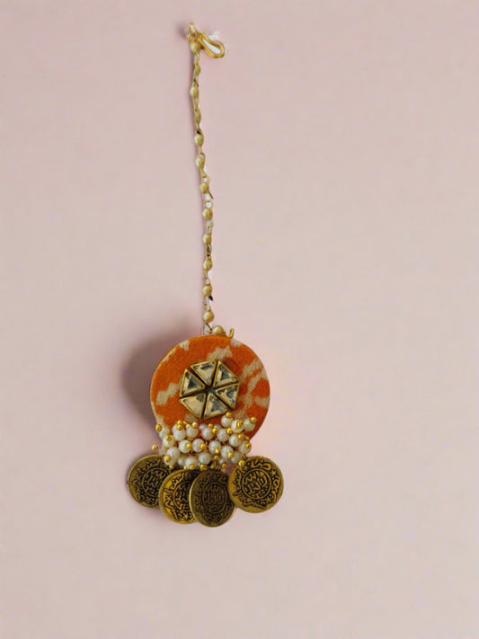 Orange patola print head locket with golden coins and white beads on white grey backdrop