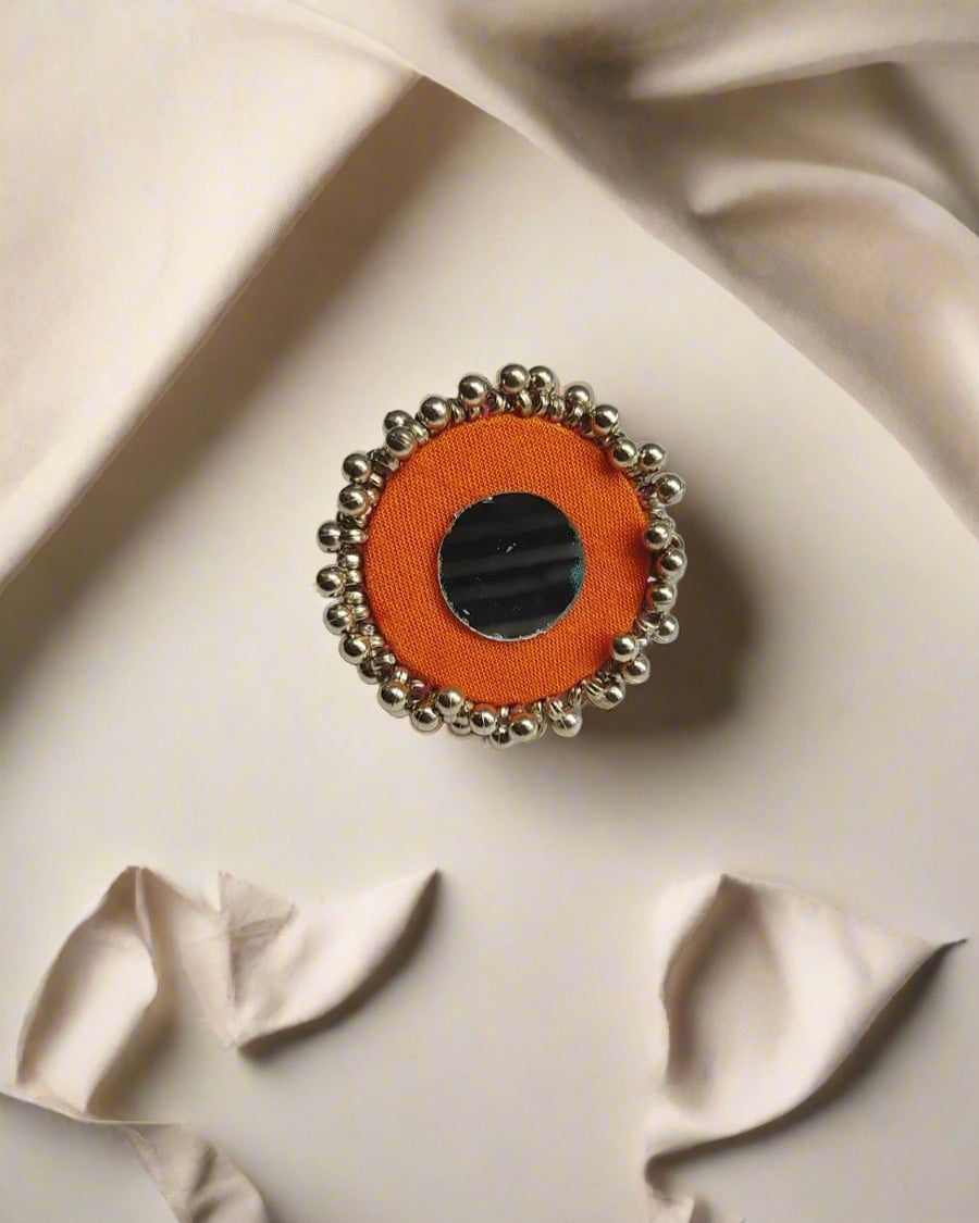 Orange round finger ring with silver beads and mirror on white backdrop