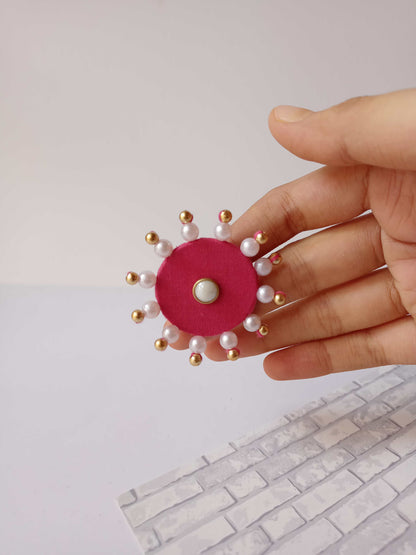 Hand holding pink round finger ring with white pearls and beads on white backdrop