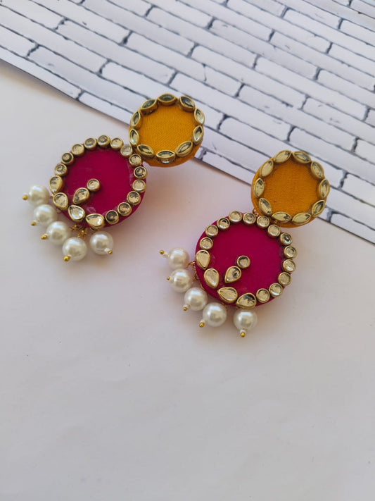 Pink and yellow round earrings with kundan border and white pearls on white grey backdrop