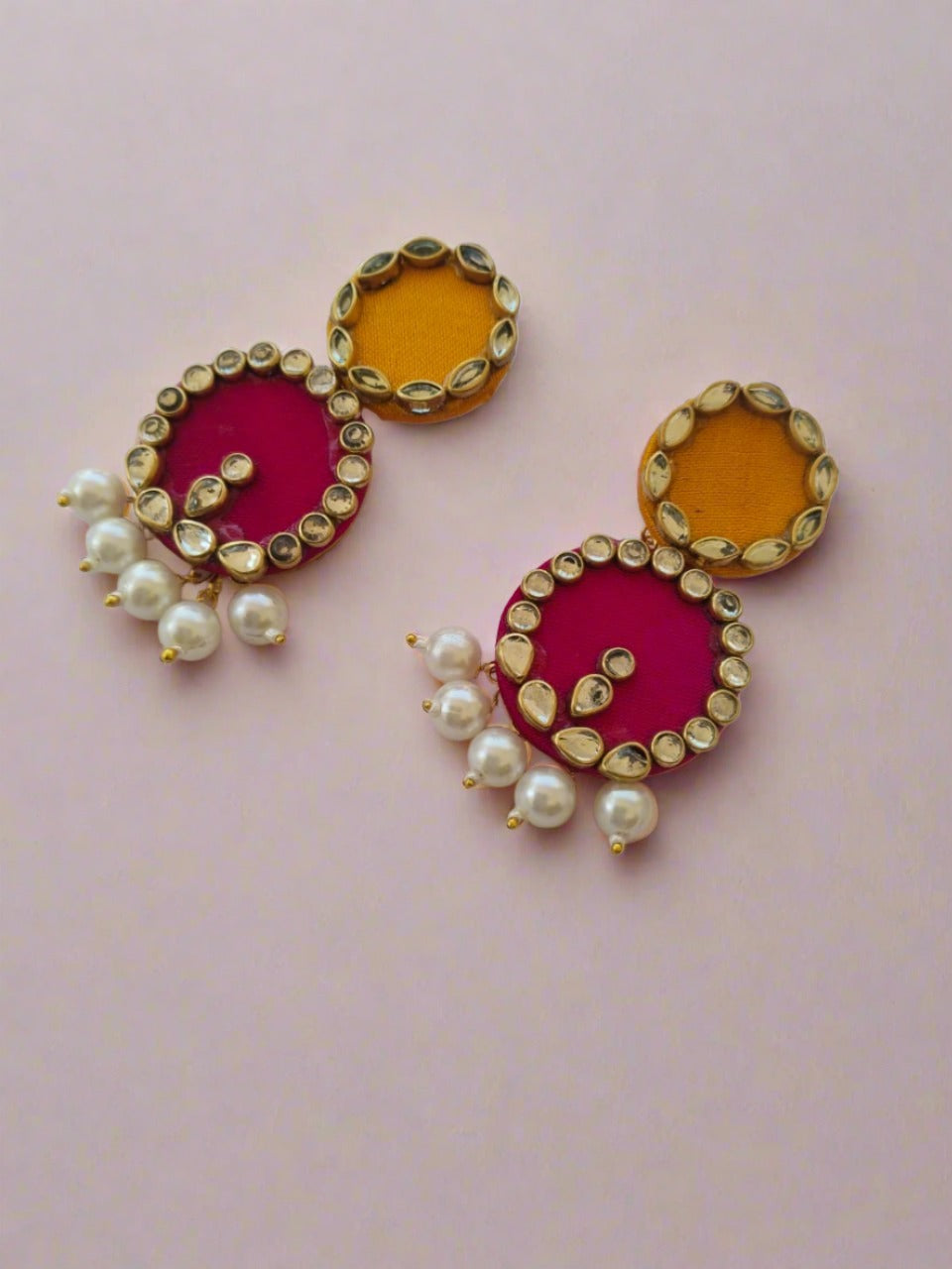 Pink and yellow round earrings with kundan border and white pearls on white grey backdrop