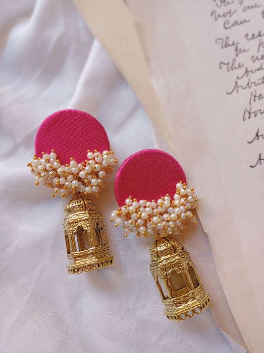 Pink jhumka errings with golden bottom on white backdrop with open book on the right
