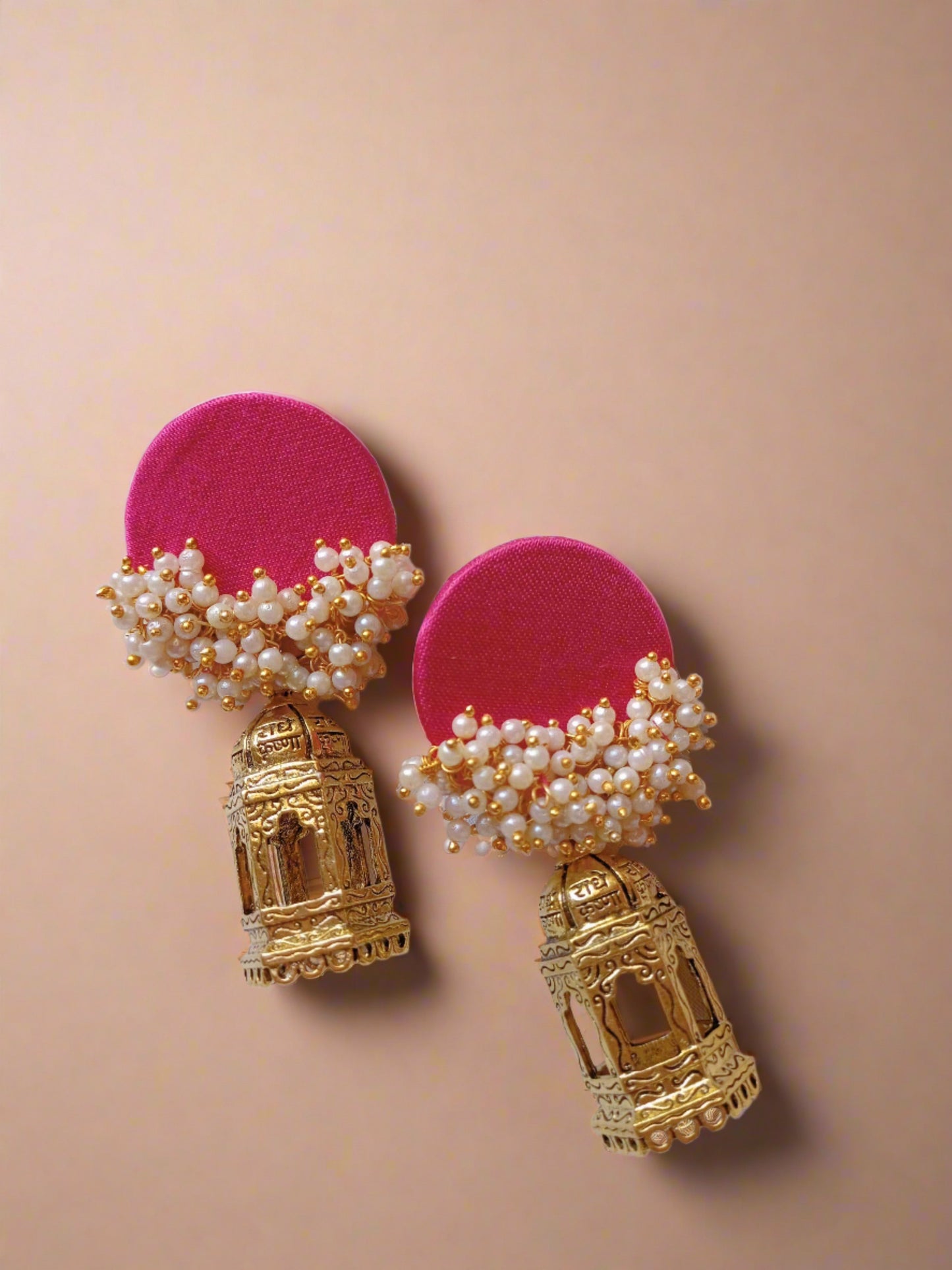 Pink jhumka errings with golden bottom on white backdrop with open book on the right