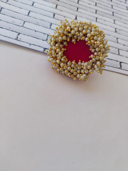 Red finger ring with white golden beads on white backdrop