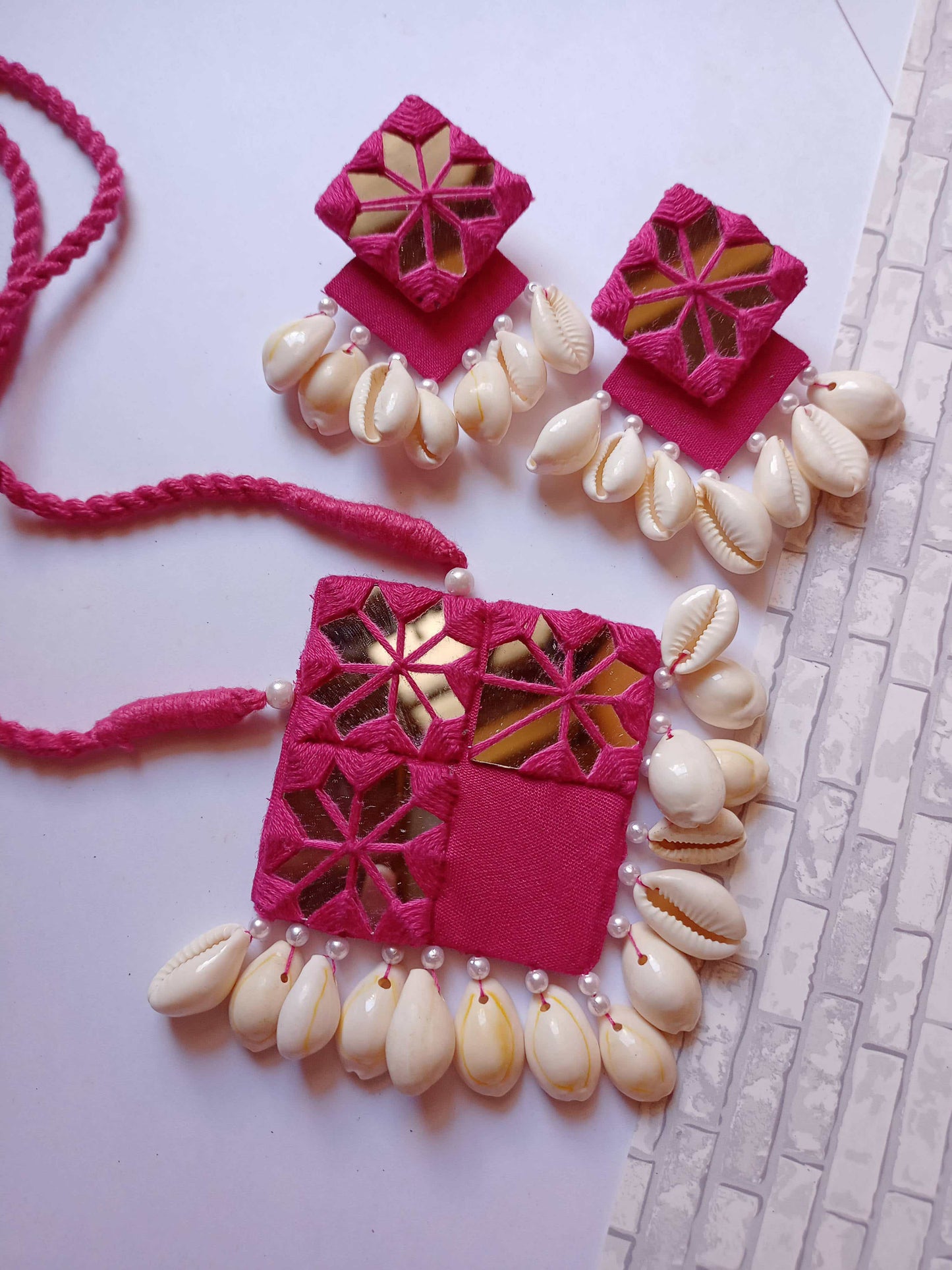 Pink square layered earrings and necklace with mirror and white sea shells on white grey backdrop