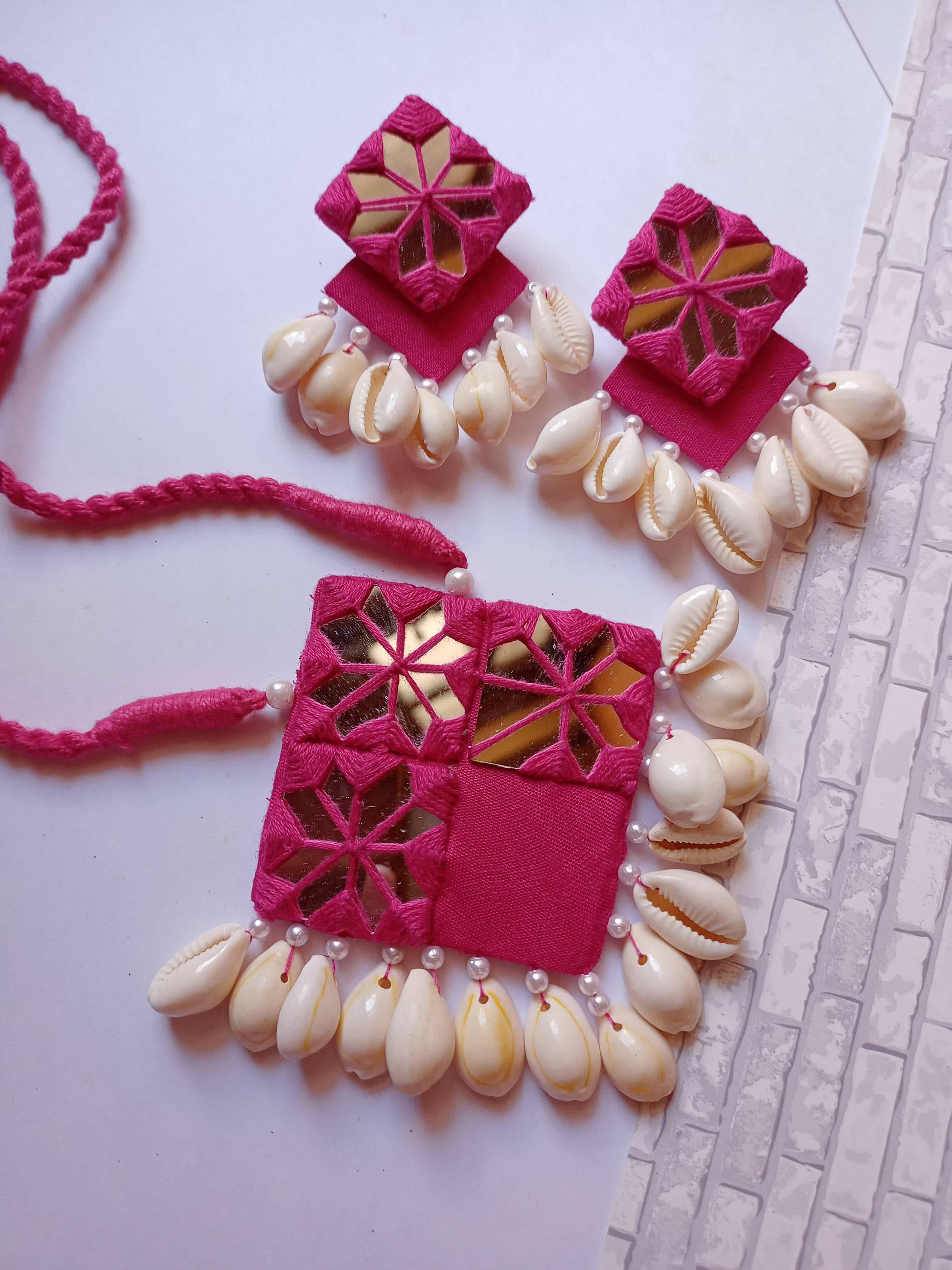 Pink square layered earrings and necklace with mirror and white sea shells on white grey backdrop