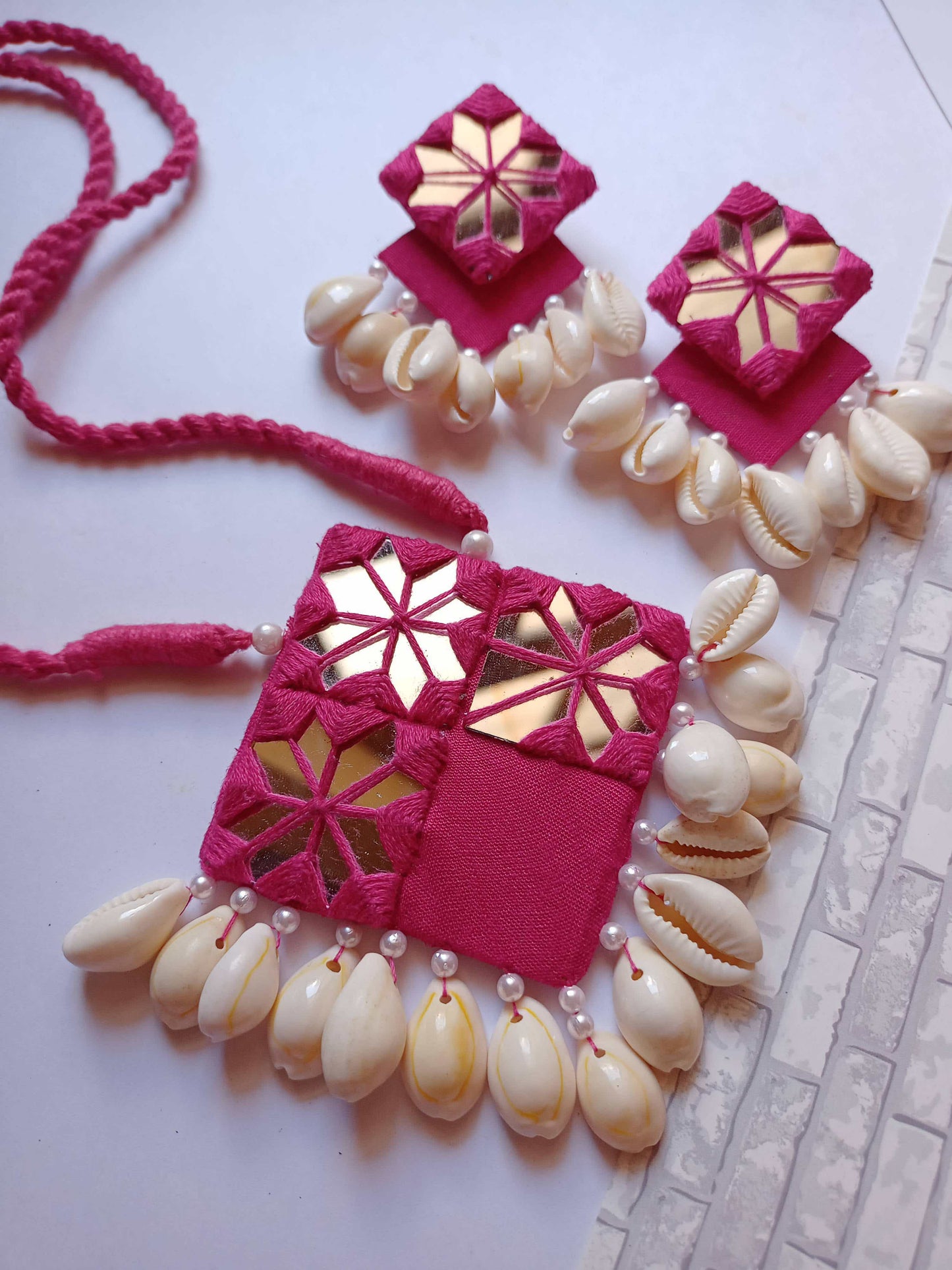 Pink square layered earrings and necklace with mirror and white sea shells on white grey backdrop