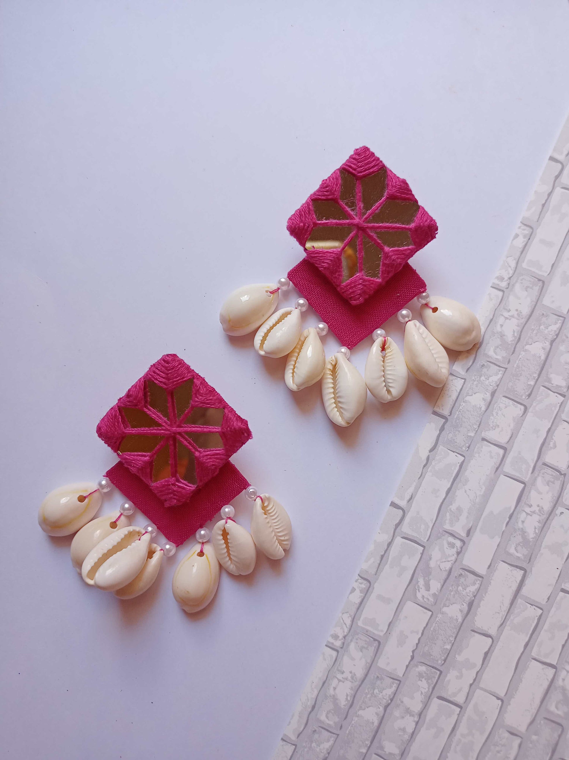 Pink square layered earrings with mirror and white sea shells on white grey backdrop