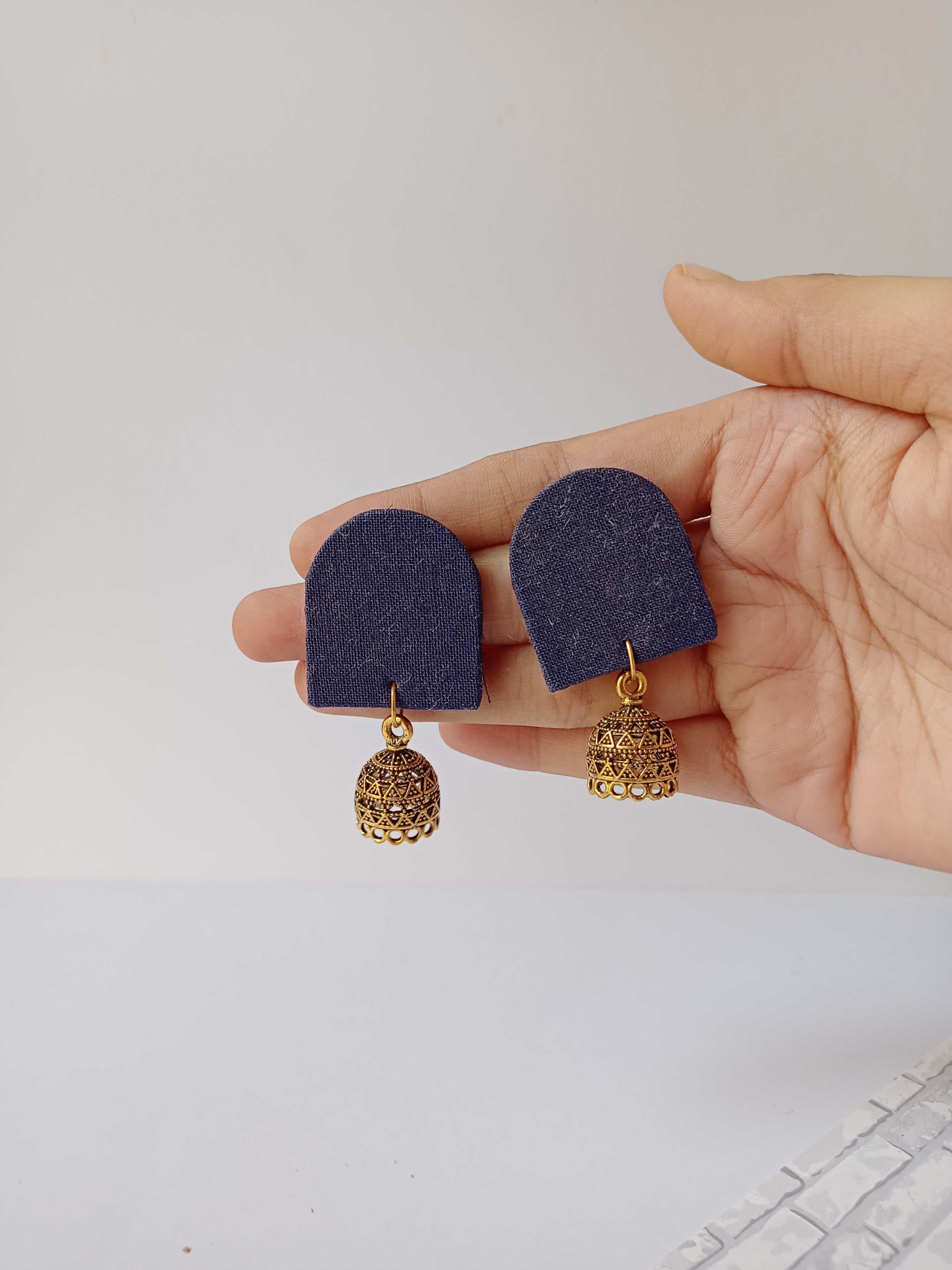 Palm holding Blue semi oval plain earrings with golden jhumki on white backdrop