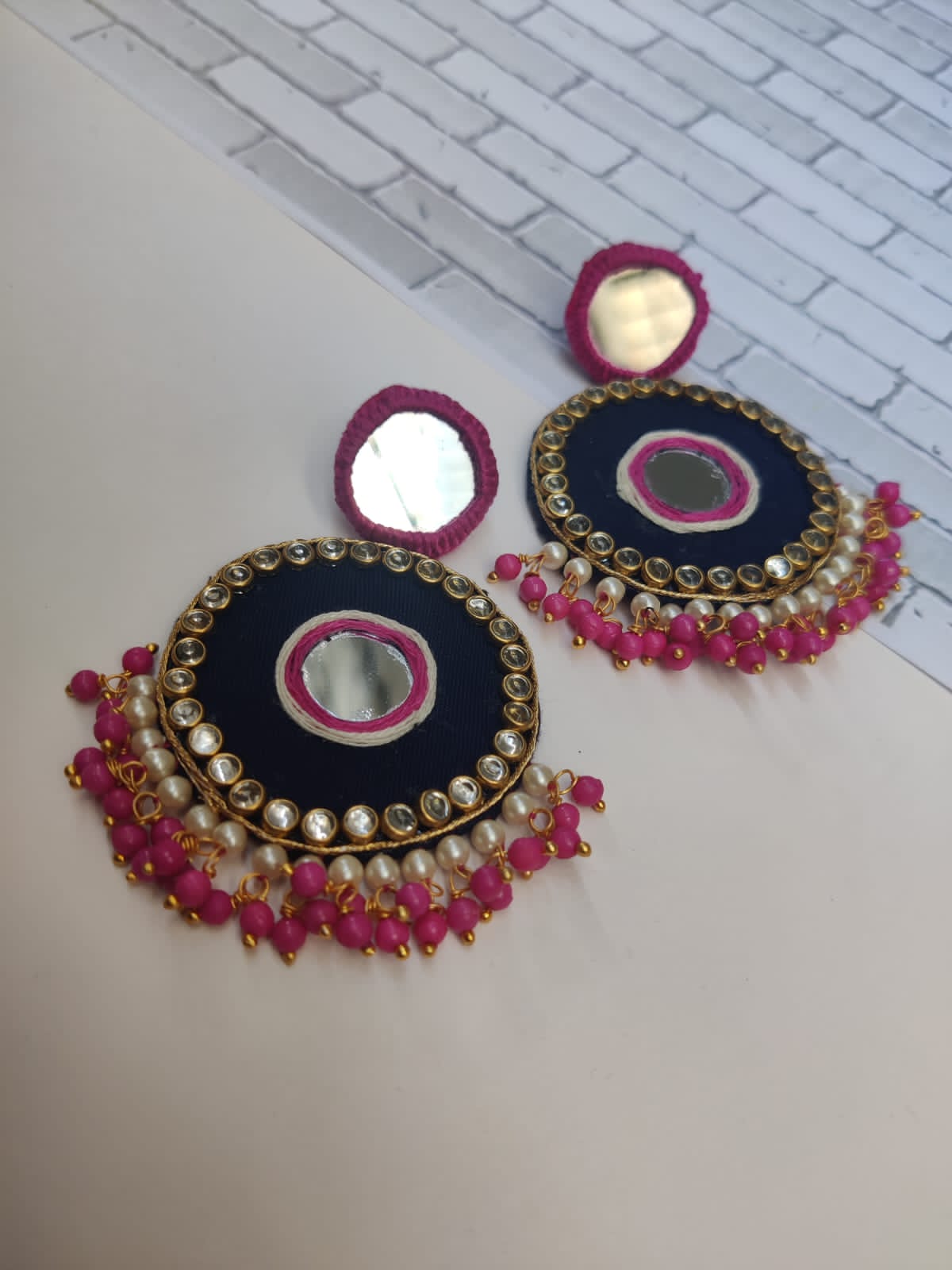 Dark pink and black mirror round earrings with beads and kundan on border on a white backdrop