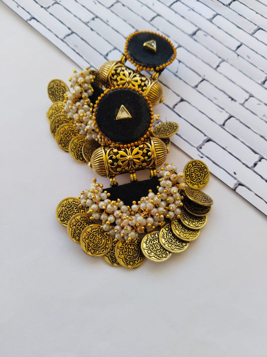 Black heavy jhumka earrings with golden tabiz and coins with white beads on white backdrop