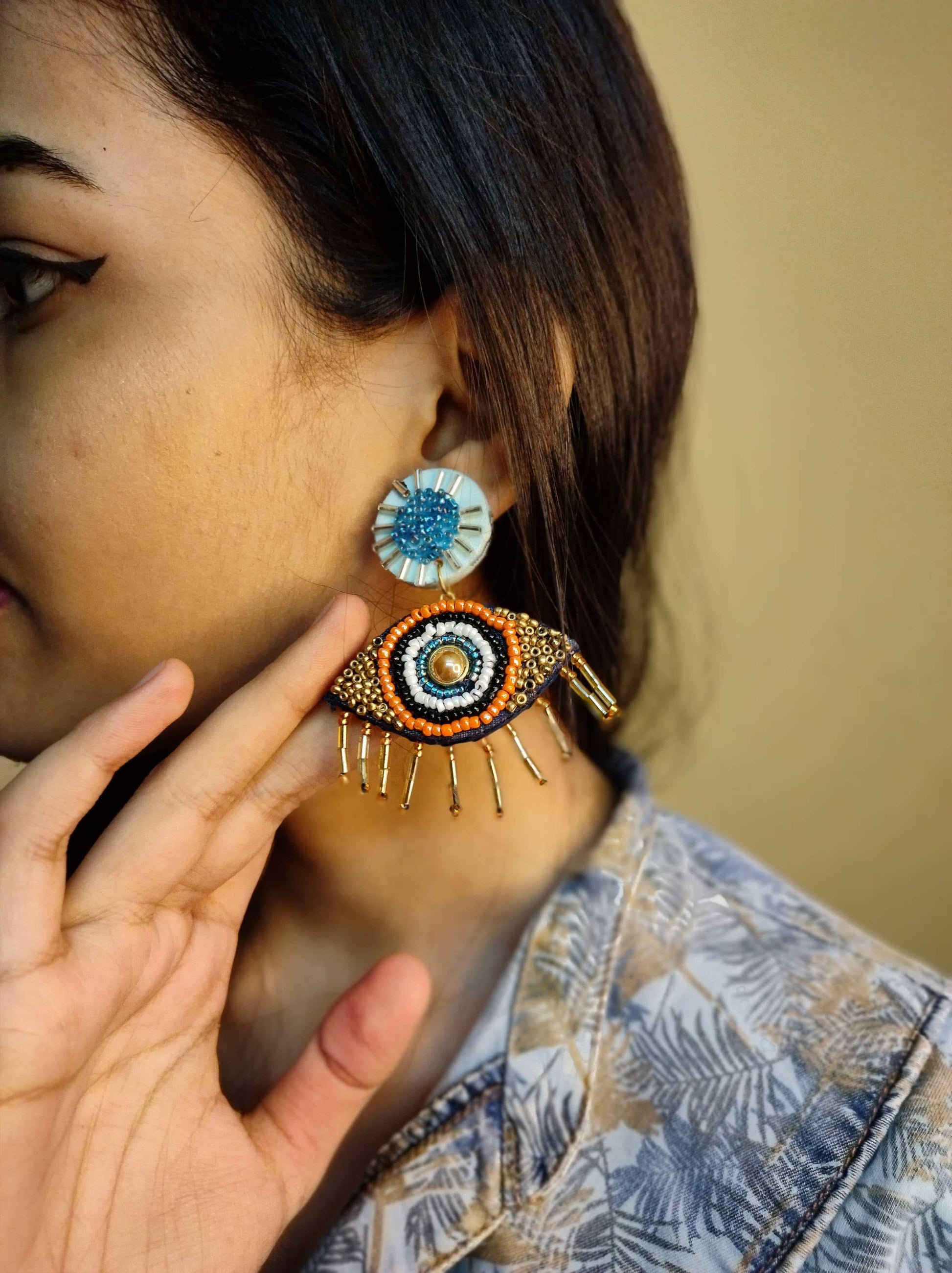 Girl wearing beaded evil eye earring on blue outfit on a yellow backdrop