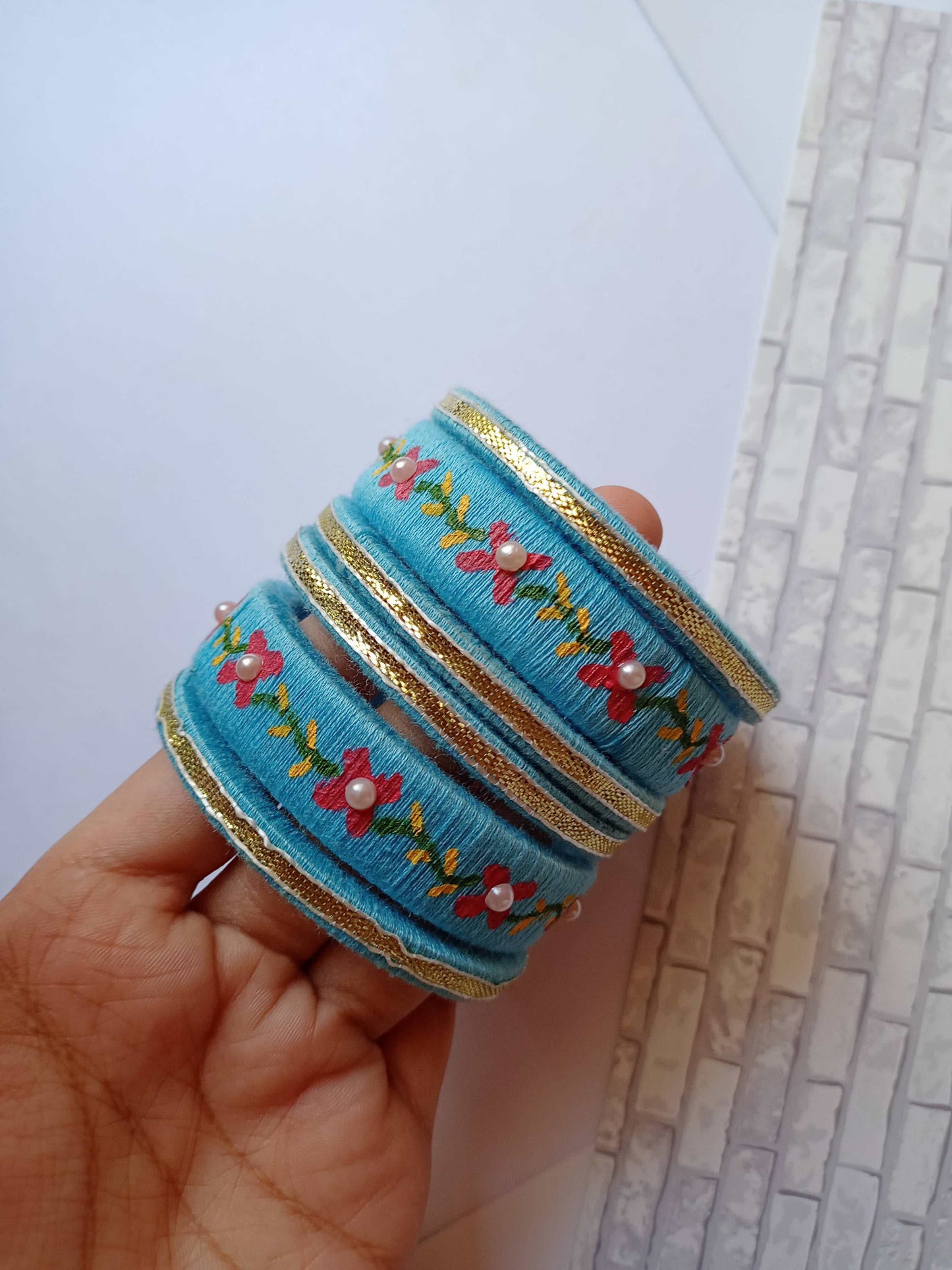 Palm holding Light blue embroidered fabric bangles set on white grey backdrop