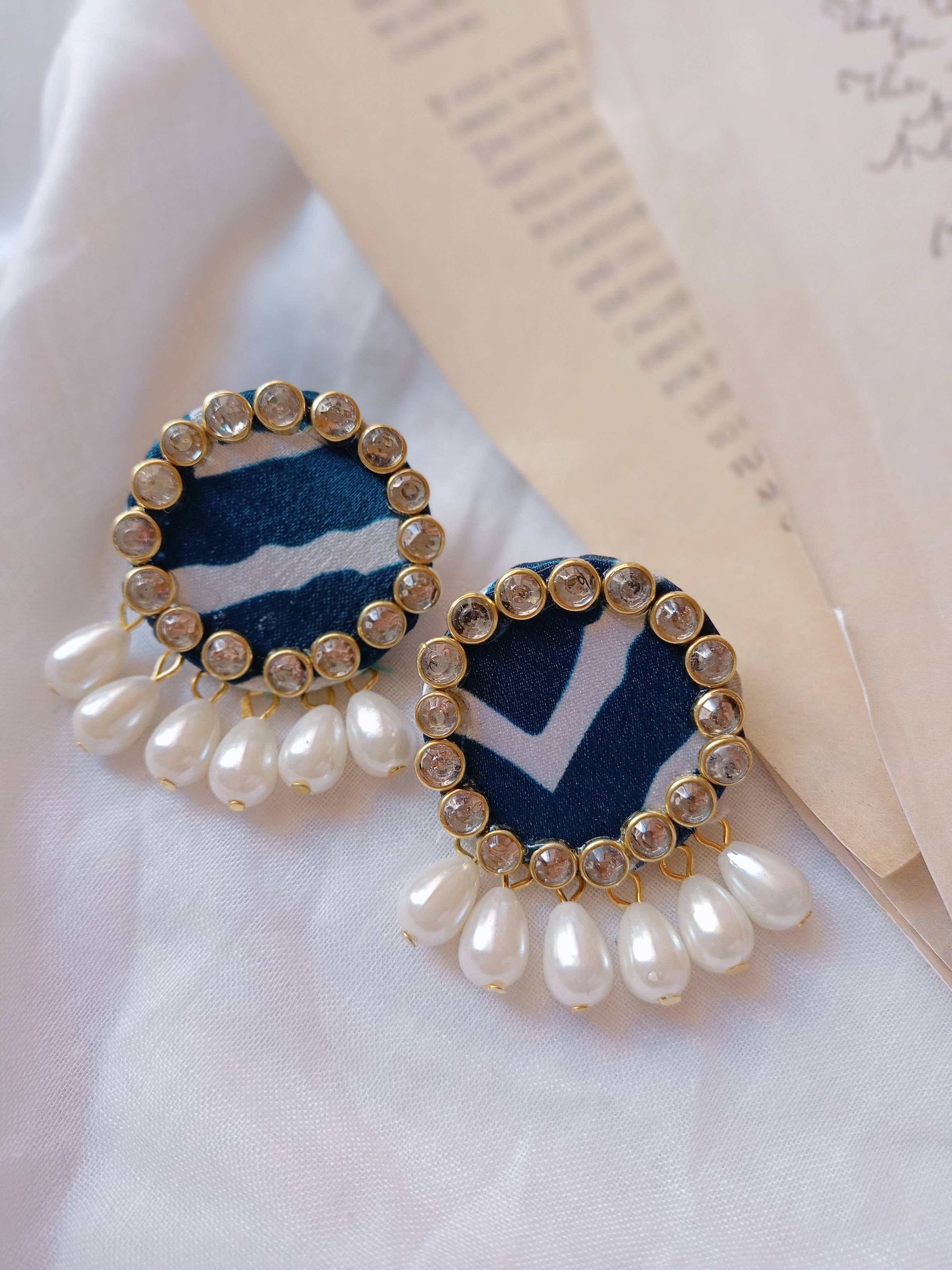 Blue printed round studs earrings with kundan border and white pearls on white backdrop
