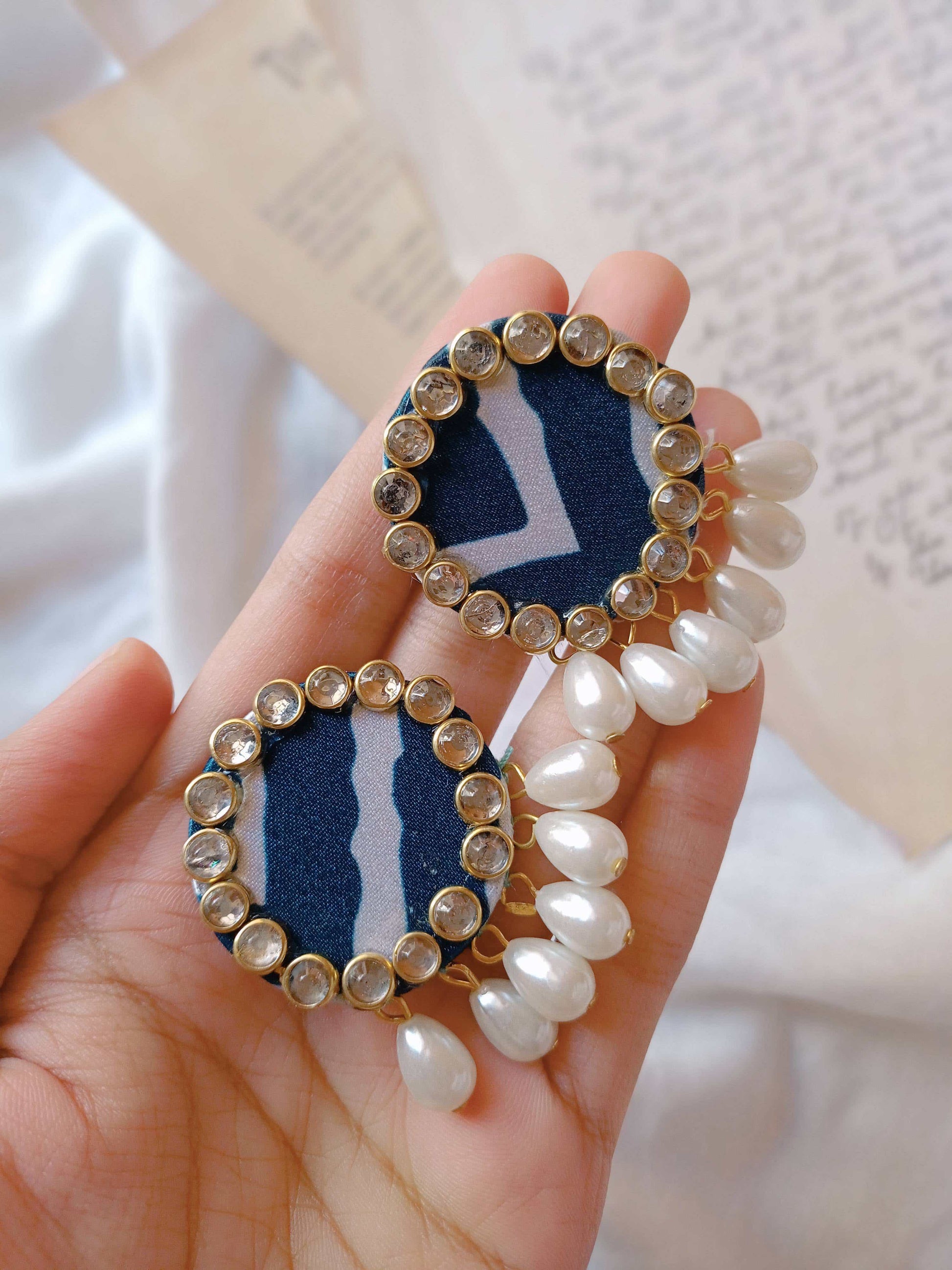 Hand holding blue printed round studs earrings with kundan border and white pearls