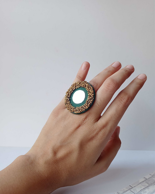 Hand wearing dark green round finger ring with mirror and golden beads border on white backdrop